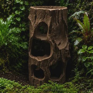 May include: A brown, cylindrical tree stump replica featuring a textured bark surface and multiple hollowed-out openings of varying sizes on the front side, designed with a hollow interior and an open top for use as a decorative garden element.