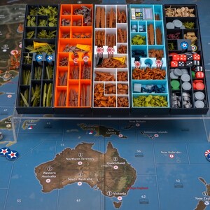 Könnte beinhalten: Ein Brettspiel-Organizer-Set mit fünf rechteckigen Fächern in Schwarz, Orange und Hellblau, die verschiedene Plastikminiaturen von Schiffen, Flugzeugen und Spielmarken enthalten. Die Fächer stehen auf einem durchsichtigen Acrylständer über einem Spielplan.