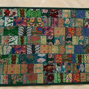 Könnte beinhalten: Ein rechteckiger Wandbehang mit einem Patchwork-Design, das aus zahlreichen kleinen, bunten Stoffquadraten besteht. Das Textil zeigt eine Vielzahl komplizierter Muster, Blumenmotive und Texturen in den Farben Grün, Blau, Rot und Gold.