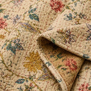 Pode incluir: Um tecido acolchoado bege com um padrão floral repetitivo em tons de vermelho, amarelo e verde. O têxtil apresenta costuras complexas em estilo kantha por toda parte, criando um efeito de grade texturizada na superfície do material.