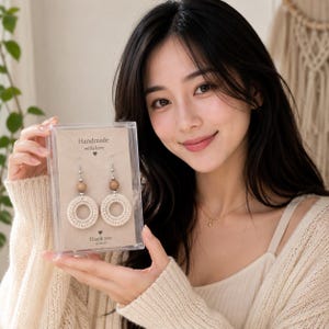 May include: A pair of cream-colored crocheted hoop earrings featuring a small wooden bead accent on a silver-toned hook. The earrings are displayed in a clear plastic box on a tan card with the text Handmade with love and Thank you so much.