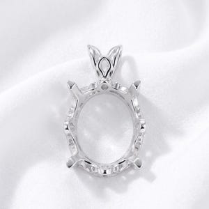 May include: A silver-toned metal pendant setting featuring an oval-shaped center frame designed to hold a gemstone. The setting includes four prongs for securing a stone and a decorative, open-work bail at the top for attaching to a necklace chain.