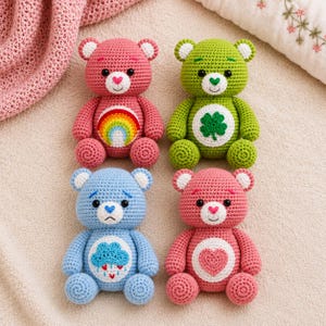May include: Four crocheted teddy bears in pink, green, blue, and coral. The pink bear has a rainbow emblem, the green bear features a four-leaf clover, the blue bear displays a rain cloud with hearts, and the coral bear has a heart symbol.