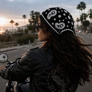 Pode incluir: Uma bandana de crochê preta com um padrão paisley branco e uma borda festonada. O acessório de cabeça é construído com pontos de fio intrincados, exibindo um motivo floral e de gota repetido por todo o design do tecido.
