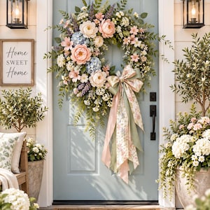 May include: A floral wreath featuring pink peonies, blue hydrangeas, and lavender sprigs, accented with green foliage and a large, multi-layered bow in sage green and floral print, hanging on a light blue door with a Home Sweet Home sign nearby.
