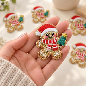 May include: A gingerbread man embroidered patch featuring a gold glitter finish, a red and white Santa hat, a red and white striped scarf, and a green Christmas tree with a yellow star. The patch has a smiling face with pink cheeks.