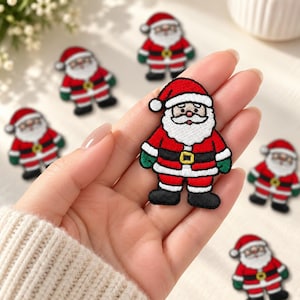May include: An embroidered Santa Claus patch featuring a red hat and suit, a white beard, a black belt with a yellow buckle, and green mittens. The patch is designed with a thick black outline and detailed stitching, showcasing a festive character.