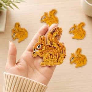 May include: A collection of squirrel-shaped patches featuring golden yellow sequins. Each patch depicts a squirrel in a seated position with a bushy tail, embroidered details for the eye and nose, and a small white accent near the mouth area.