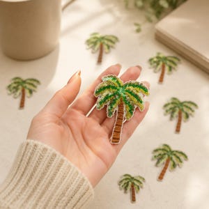 May include: A palm tree patch featuring green and yellow sequins for the fronds and brown thread for the trunk. The patch has a white embroidered border. Several identical palm tree patches are scattered around the central palm tree patch.