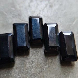 May include: Five rectangular black gemstones with faceted edges arranged in a slight arc. Each stone features a smooth, polished surface with a deep, dark color and sharp, clean geometric lines that reflect light along the beveled borders.