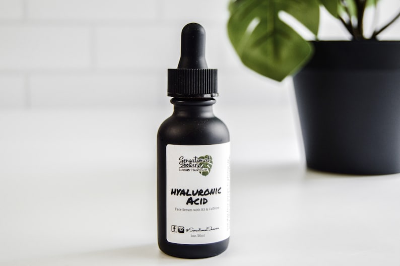 Puede incluir: Botella de vidrio negro con cuentagotas, etiquetada como "HYALURONIC ACID Face Serum with B3 & Caffeine". La botella tiene una etiqueta blanca con el nombre de la marca y un dise&ntilde;o de hoja verde. La botella es de 30 ml.