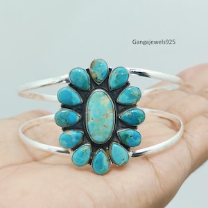 May include: A silver cuff bracelet featuring a central oval turquoise stone surrounded by eleven smaller pear-shaped turquoise stones in a floral arrangement. The metal band is smooth and polished. The text Gangajewels925 is visible in the corner.