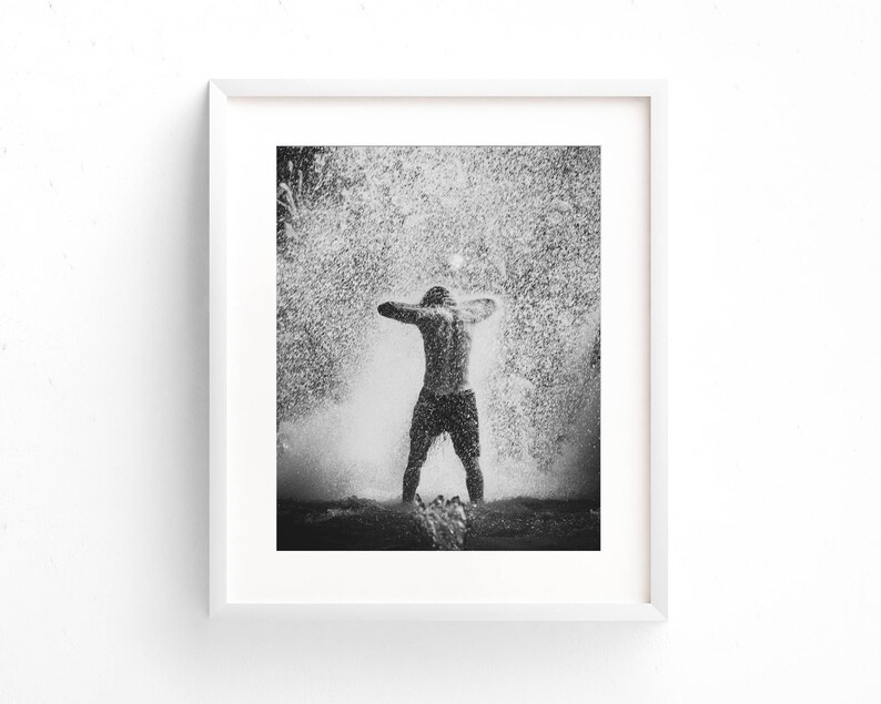 May include: A black and white photograph of a person standing in a fountain with water splashing around them.