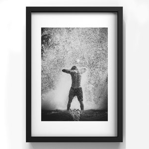 May include: A black and white photograph of a person standing in a fountain with water spraying up around them.