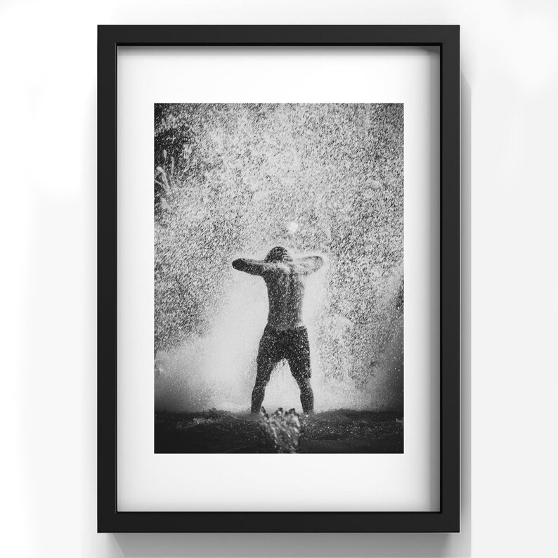 May include: A black and white photograph of a person standing in a fountain with water spraying up around them.