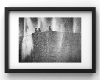 May include: Black and white photograph of three people silhouetted against a background of water fountains. The people are sitting on a ledge, and the water fountains are spraying up into the air.