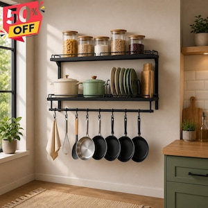 Puede incluir: Un estante de cocina de pared de dos niveles hecho de metal negro, con una repisa superior para cinco frascos de vidrio, una repisa central con dos ollas, platos y tablas de cortar, y una barra inferior con ganchos para colgar sartenes.