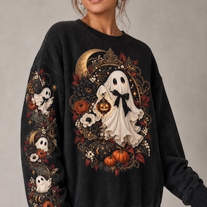 May include: A black long-sleeve sweatshirt featuring a graphic print of a white ghost holding a glowing lantern, surrounded by an ornate frame, autumn leaves, flowers, and pumpkins. The sleeve also displays a vertical pattern of smaller ghosts.