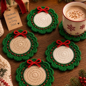 Puede incluir: Cuatro posavasos redondos de ganchillo con centro color crema, borde festoneado verde y un pequeño lazo de hilo rojo en la parte superior. Un posavasos sostiene una taza de cerámica blanca con copos de nieve rojos y una etiqueta que dice Handmade Happiness in Every Stitch.