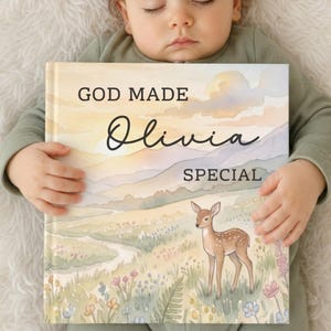 May include: A hardcover book titled God Made Olivia Special featuring a watercolor illustration of a fawn in a meadow with mountains and a sunset sky. The book cover displays soft pastel colors including yellow, orange, blue, and green tones.