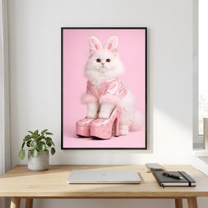 Könnte beinhalten: Ein gerahmter Wandkunstdruck, der eine flauschige weiße Katze mit rosa Hasenohren und einer passenden rosa Satinjacke mit Fellbesatz zeigt. Die Katze steht mit ihren Vorderpfoten in einem Paar hellrosa Plateauschuhen mit hohem Absatz.