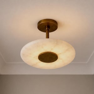 May include: A flush mount ceiling light fitting featuring a circular, translucent white alabaster shade with natural veining. The fitting includes a central brass-toned metal disc and a matching cylindrical stem connecting to a circular brass ceiling canopy.