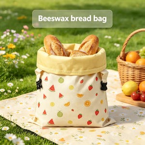 May include: A cream-colored beeswax bread bag featuring a repeating pattern of strawberries, watermelon slices, orange segments, and melons. The bag has a yellow interior lining, black side buckles, and contains three crusty loaves of bread.