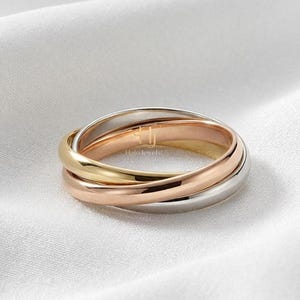 Può includere: Un anello a tre fasce intrecciate in oro giallo, oro rosa e metallo color argento. L'anello presenta il testo HaloJewelsUS inciso sulla superficie della fascia in oro giallo, mostrando una finitura liscia e lucida su tutte le bande.