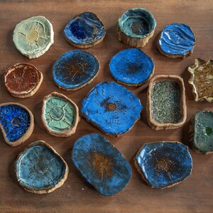 May include: A collection of fifteen small, handcrafted ceramic dishes with irregular, organic shapes. The pieces feature varied glazed finishes in shades of deep blue, turquoise, brown, and green, with some showing textured, crackled, or cratered surfaces.