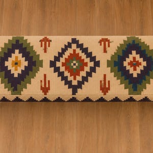 May include: A rectangular upholstered bench featuring a cream-coloured fabric top with a repeating geometric pattern in navy blue, forest green, burnt orange, and yellow. The bench is supported by four dark brown turned wooden legs.