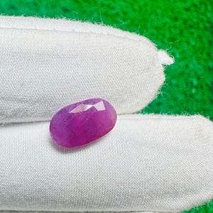以下が含まれることがあります： 鮮やかなマゼンタピンク色の楕円形でファセットカットされた宝石。石の表面は研磨されており、幾何学的なファセットが光を反射し、その半透明の質感と深く飽和した色合いを明確な形状で際立たせています。