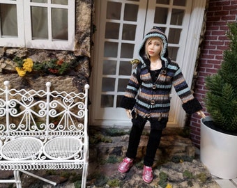 May include: A doll with blonde hair wearing a hooded, long-sleeved cardigan featuring horizontal stripes in shades of blue, brown, and black. The cardigan has a black hood trim, black cuffs, and three front buttons. The doll wears black pants and pink shoes.