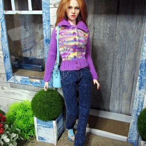 May include: A doll wearing a purple and yellow striped cardigan with a light blue purse, blue jeans, and light blue sandals.