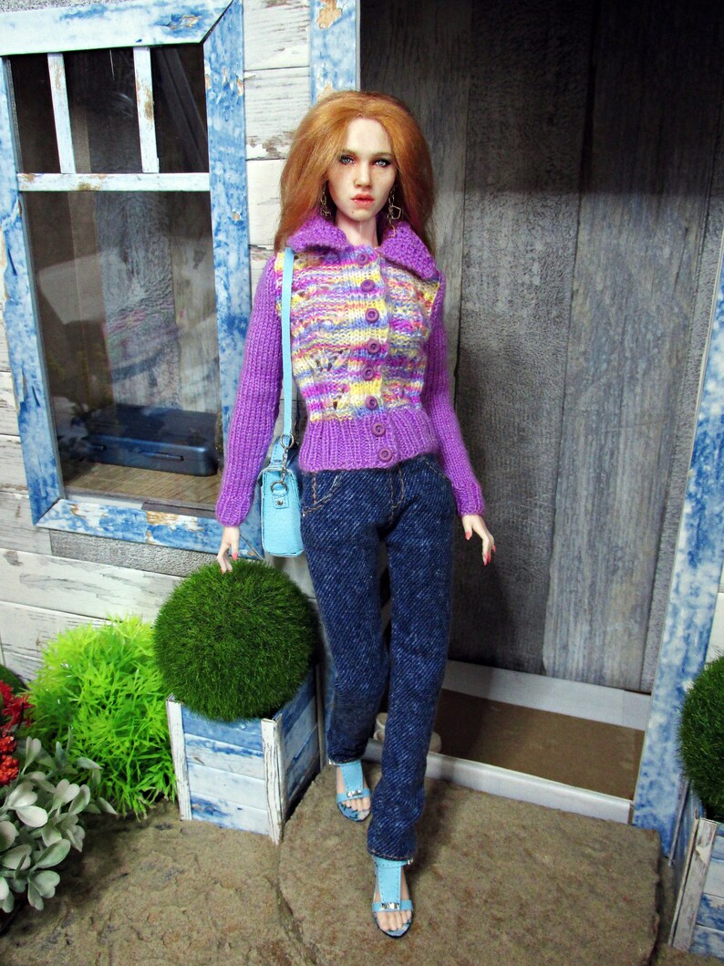 May include: A doll wearing a purple and yellow striped cardigan with a light blue purse, blue jeans, and light blue sandals.
