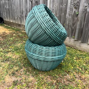 May include: Two stacked teal-coloured woven baskets with a rounded, bowl-like shape. The baskets feature a detailed lattice pattern created by interlaced strips, forming a sturdy structure with a consistent, smooth finish across the entire surface.