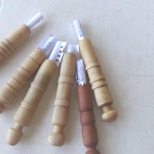 May include: Six cylindrical wooden handles arranged in a fan shape, each featuring a small white paper insert at the top. Five handles are light tan wood with ribbed detailing, while one handle is a darker brown wood with a similar ribbed design.