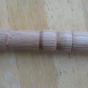 Puede incluir: Un mango de madera clara, posiblemente de roble, con una serie de secciones redondeadas. El mango tiene patrones de vetas visibles. El diseño sugiere un mango de herramienta o utensilio.