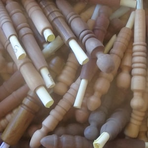 Könnte beinhalten: Eine Kiste voller Holzspindeln in verschiedenen Hell- und Dunkelbrauntönen. Einige Spindeln haben eine zylindrische Form, andere dekorative gedrehte Designs. Jede Spindel hat eine weiße Papierspitze.