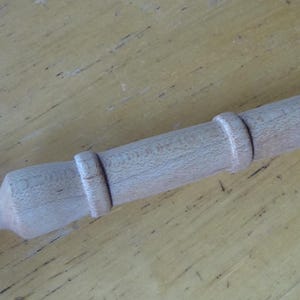 May include: A wooden dowel rod with a rounded end and two decorative rings. The rod is light brown in color.