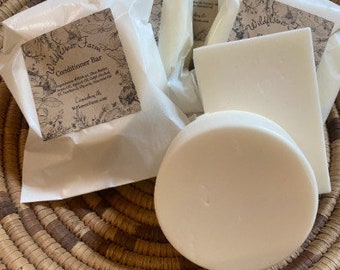 May include: A set of four white conditioner bars wrapped in white paper with a floral design and the text "Wildflower Farm Conditioner Bar".