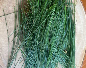 May include: A close-up of a pile of long, thin, green pine needles on a wooden surface.