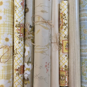 May include: A collection of vintage wallpaper rolls with various patterns and colors, including floral, geometric, and abstract designs. The rolls are tied with twine and appear to be in good condition.