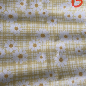May include: A yellow fabric with a white daisy pattern. The fabric has a subtle checkered pattern.