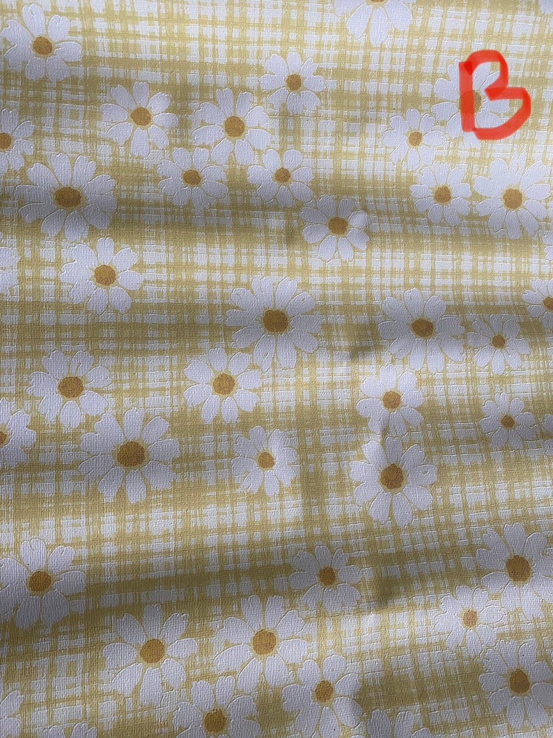 May include: A yellow fabric with a white daisy pattern. The fabric has a subtle checkered pattern.