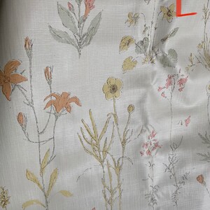 May include: A white fabric with a floral pattern featuring various shades of pink, yellow, and orange flowers. The fabric has a subtle linen texture.