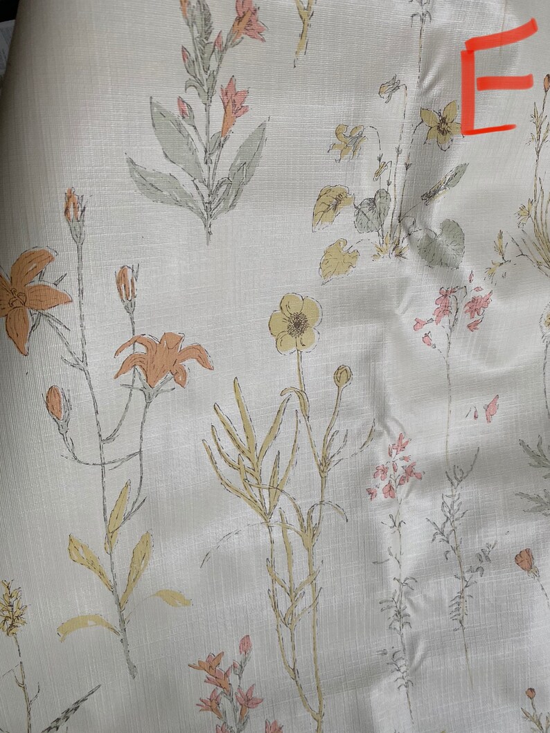 May include: A white fabric with a floral pattern featuring various shades of pink, yellow, and orange flowers. The fabric has a subtle linen texture.