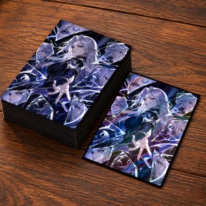 May include: A stack of rectangular trading card sleeves and one individual sleeve featuring an illustration of a character with long white hair, dark clothing, and a glowing hand, set against a background of dark blue, shattered glass-like shards.