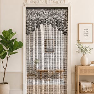 May include: A doorway curtain featuring a black lace valance with a scalloped edge and intricate floral patterns, hanging above a series of vertical beaded strands in alternating black and white colors that create a linear, striped visual effect.