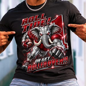 May include: A black short-sleeve t-shirt featuring a graphic of a muscular grey elephant wearing red and white sports gear, holding a football. The text reads ROLL TIDE! OR GET ROLLED OVER!! with a large number one in the background.