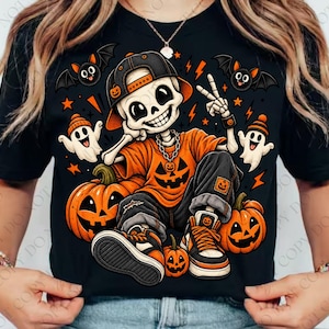 May include: A black t-shirt featuring a graphic of a smiling skeleton wearing a baseball cap, an orange shirt with a jack-o'-lantern face, and sneakers. The skeleton is surrounded by two small ghosts, two bats, and three pumpkins, all set against a black background.